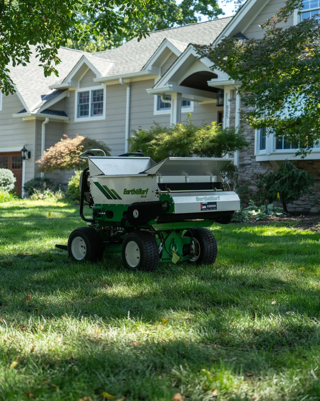 GreenStripe's Earth & Turf 420 SP compost topdresser parked on a sunlit front lawn in front of a New Jersey home