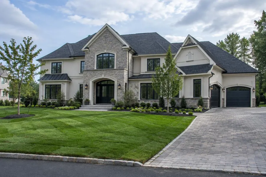 Newly built stone and stucco home with freshly laid sod, young trees and a paver driveway in Short Hills, NJ