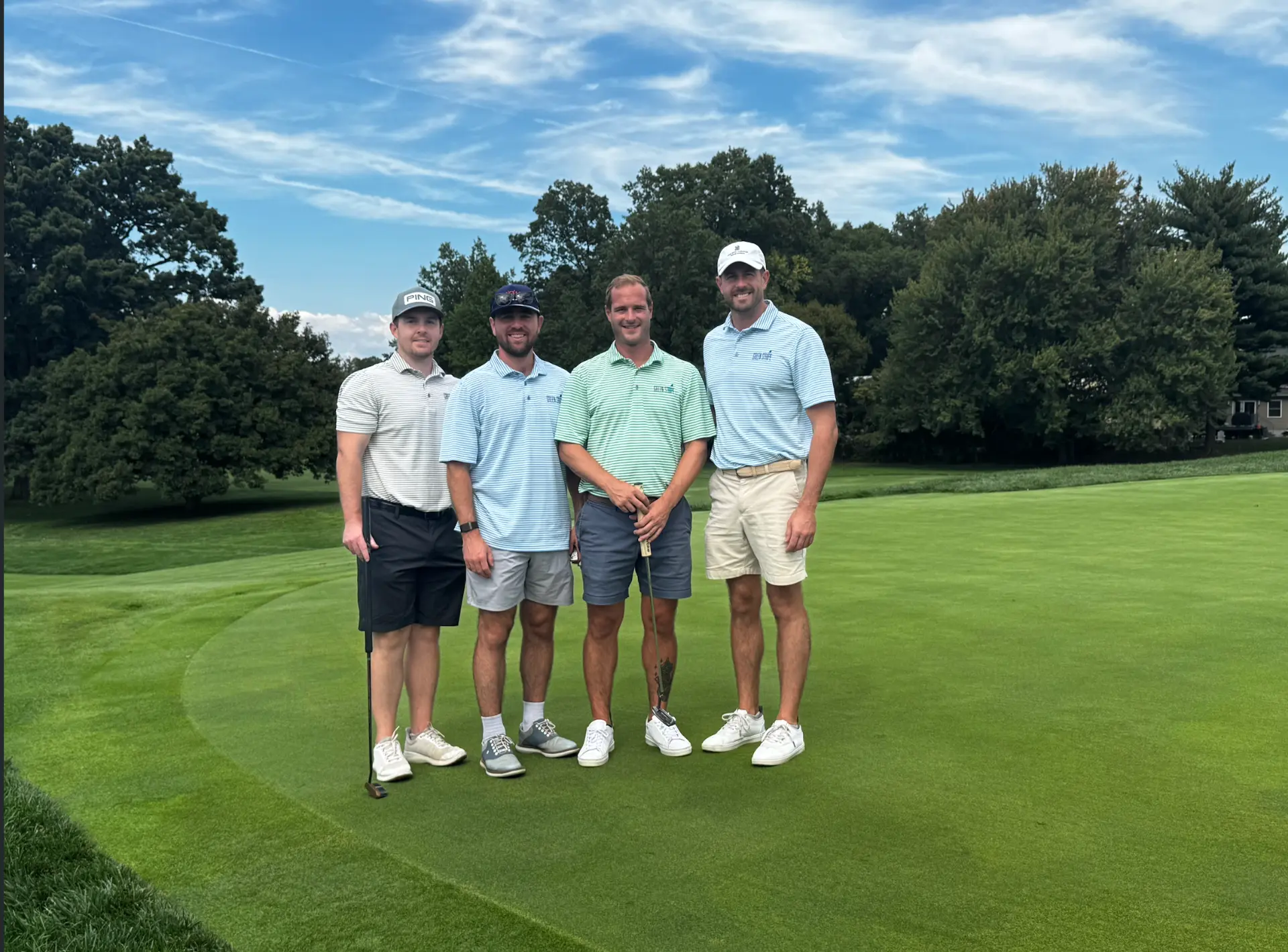Four GreenStripe team members in company polos on a golf course green