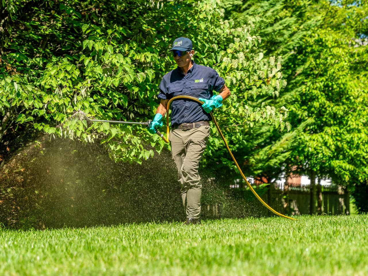 GreenStripe lawn technician Oscar in uniform spraying a liquid biological soil treatment with a hose and spray wand across a green front lawn in Northern New Jersey