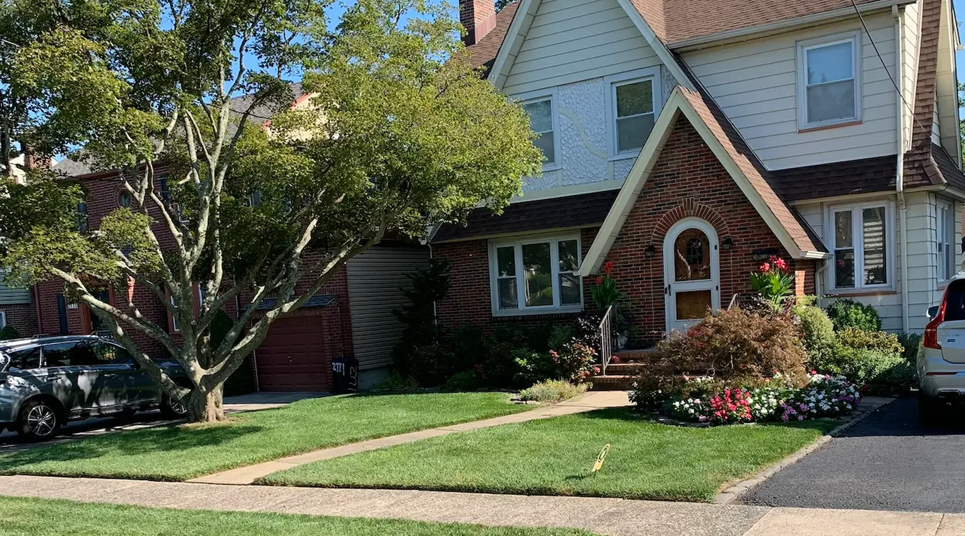 Brick-and-siding Tudor-style home with a thick, freshly mowed front lawn, mature tree and colorful flower beds in Union, NJ