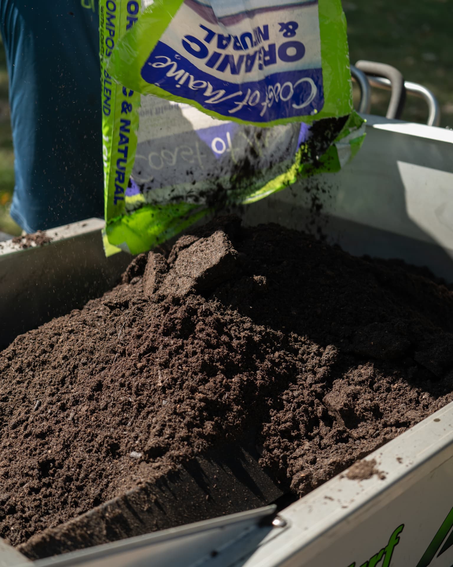 Organic compost being poured into a GreenStripe topdressing spreader