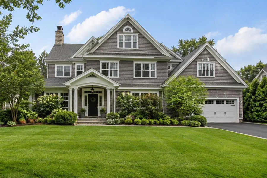 Cedar-shingle home with a covered entry, established foundation landscaping and a thick manicured front lawn in Short Hills, NJ
