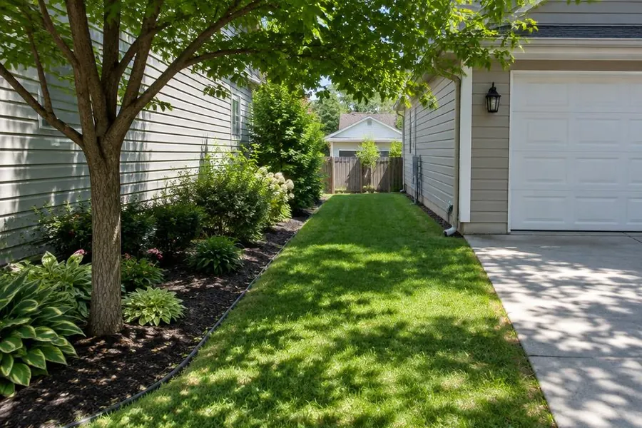 Narrow side-yard lawn between a house and driveway, shaded by a tree and bordered by a landscape bed in Roselle Park, NJ