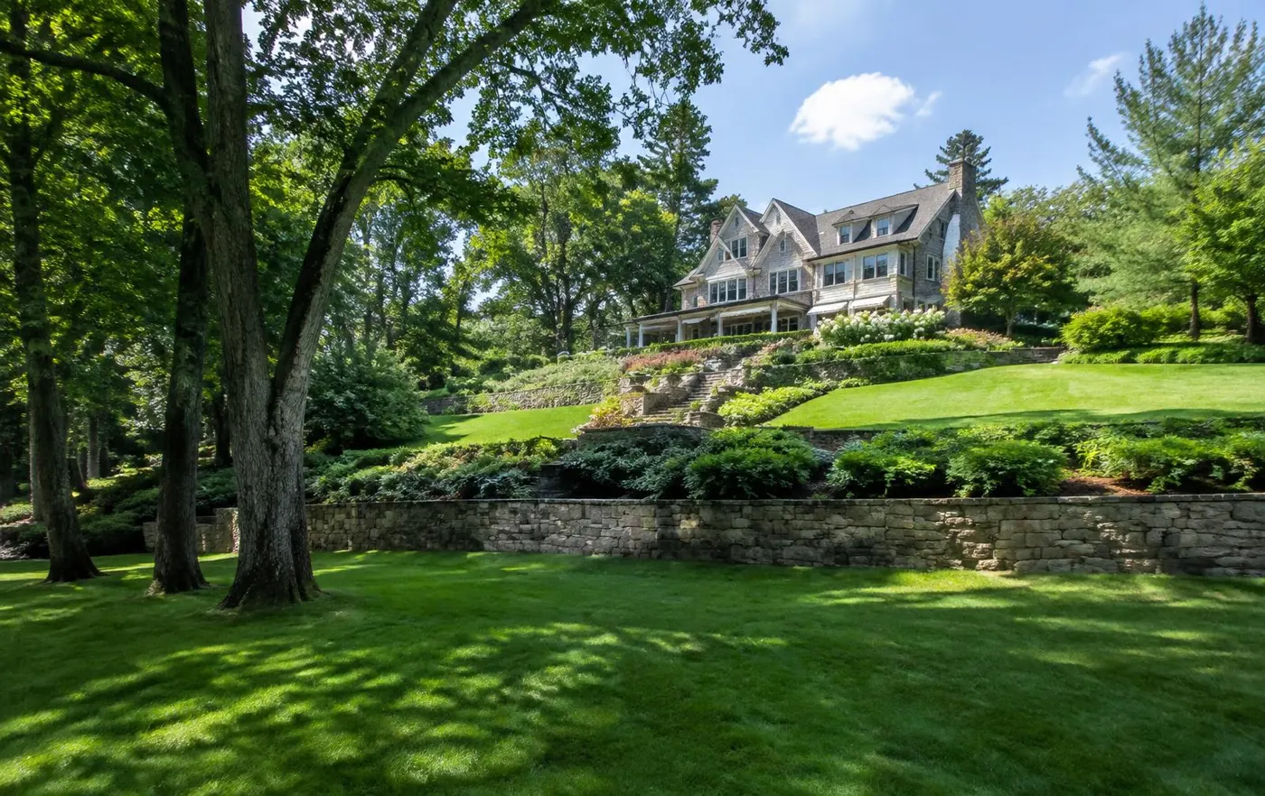 Hillside property with sunny upper lawn terraces, stone walls and stairs, and a shaded lower lawn beneath large trees in Short Hills, NJ