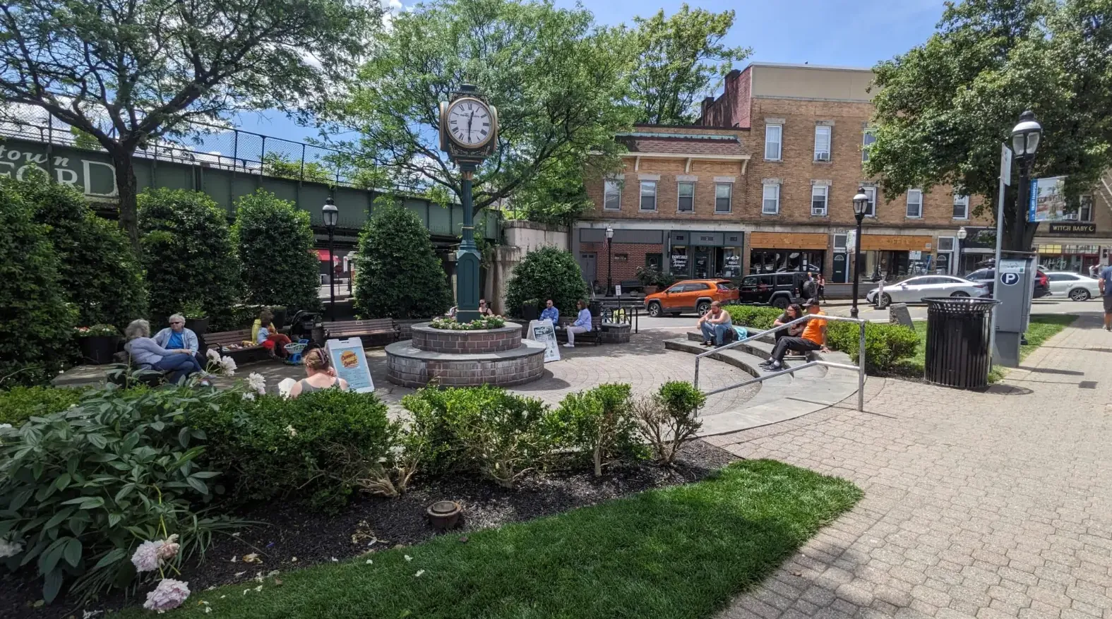Clock plaza in Downtown Cranford, NJ with a freshly cut lawn, shrub beds and brick storefronts