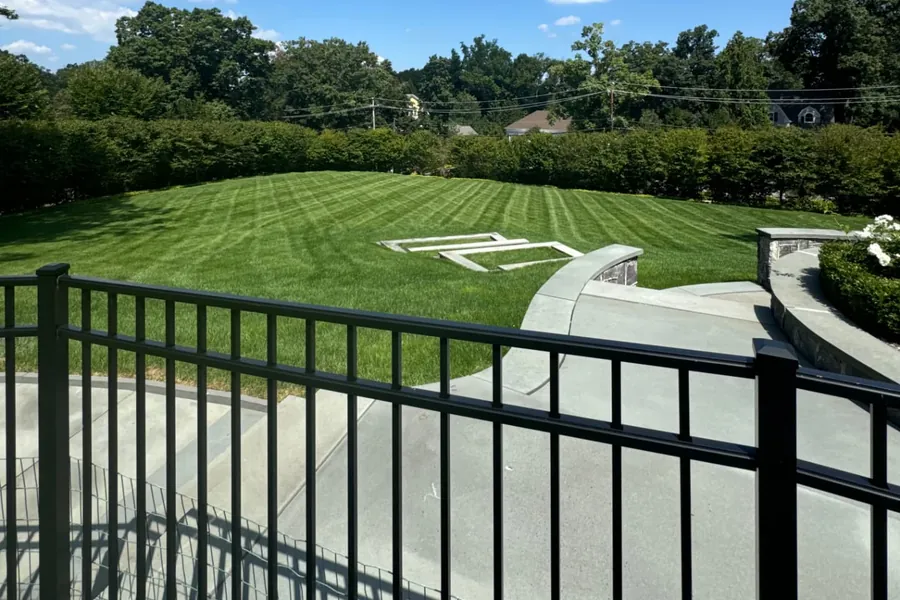 Large striped backyard lawn below a curved stone terrace, framed by tall hedges and mature trees in Summit, NJ