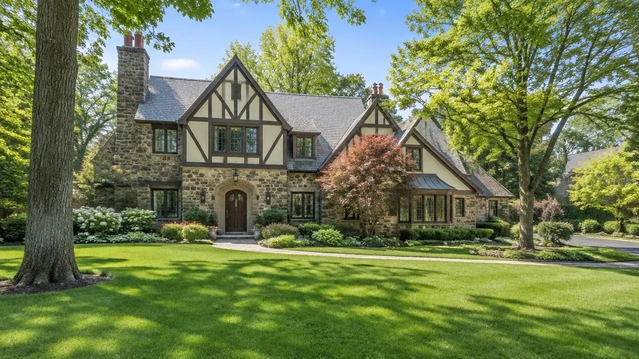 Stone and stucco Tudor-style home with a thick green front lawn, Japanese maple and mature trees in Millburn, NJ