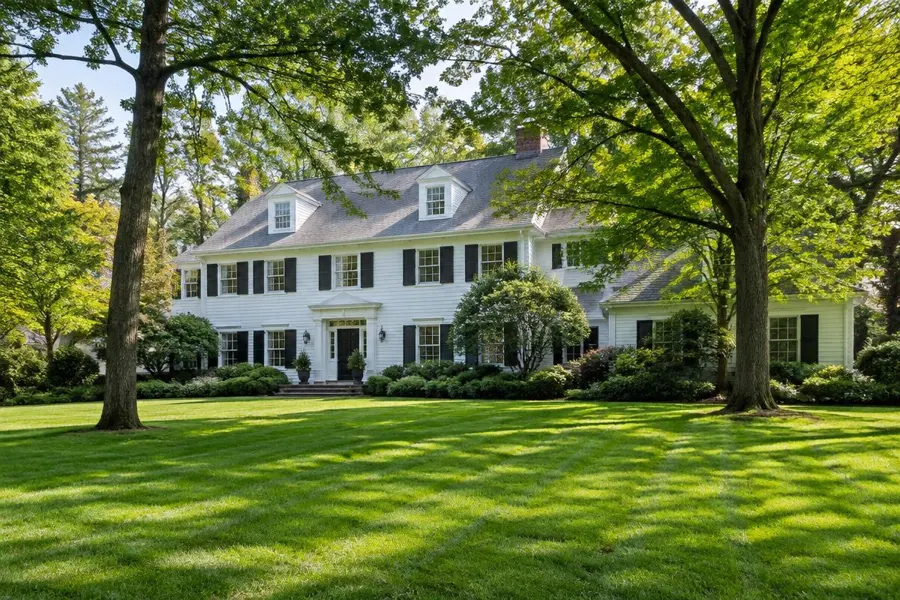 Large striped front lawn beneath tall trees at a white colonial home in Mountainside, NJ