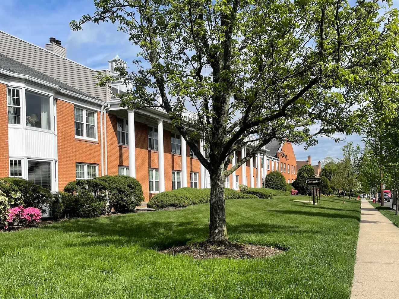 Colonial brick apartment complex with white columns, a thick, freshly mowed green lawn, shade tree and azaleas maintained by GreenStripe in Westfield, NJ