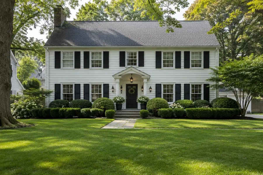 White center-hall colonial home with black shutters, rounded boxwoods and a thick, mature front lawn in Chatham, NJ