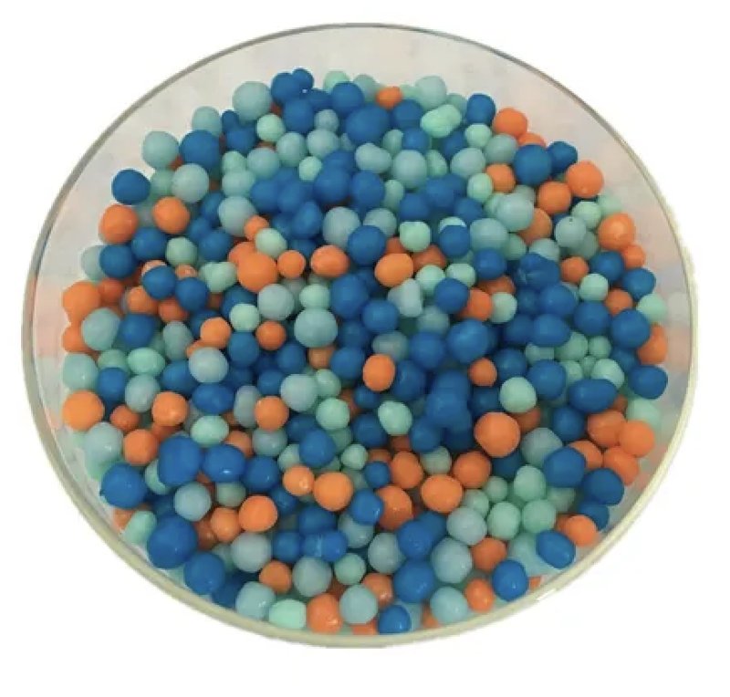 Poly-coated plastic urea fertilizer prills in blue, light green and orange in a glass dish, showing polymer-coated slow-release lawn fertilizer