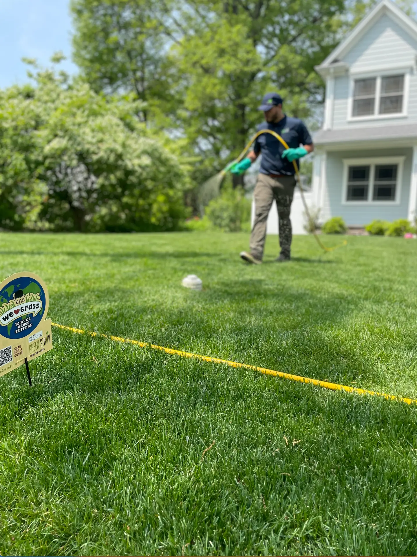 GreenStripe technician hose-treating a front lawn beside a GreenStripe yard sign