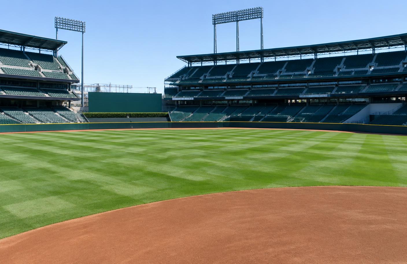 Empty major league baseball stadium with a bright green, checkerboard-striped natural grass outfield on a sunny spring morning