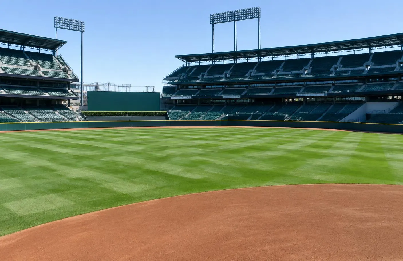 Empty major league baseball stadium with a bright green, checkerboard-striped natural grass outfield on a sunny spring morning