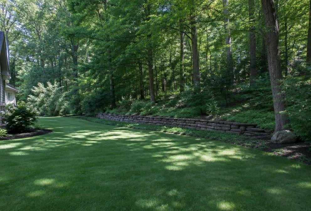 Manicured lawn meeting a wooded tree line behind a stone retaining wall